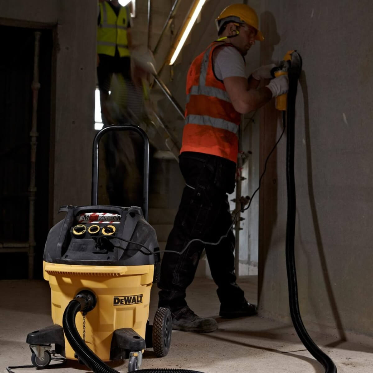 A worker using a power tool with a Dewalt extractor attached in a construction setting